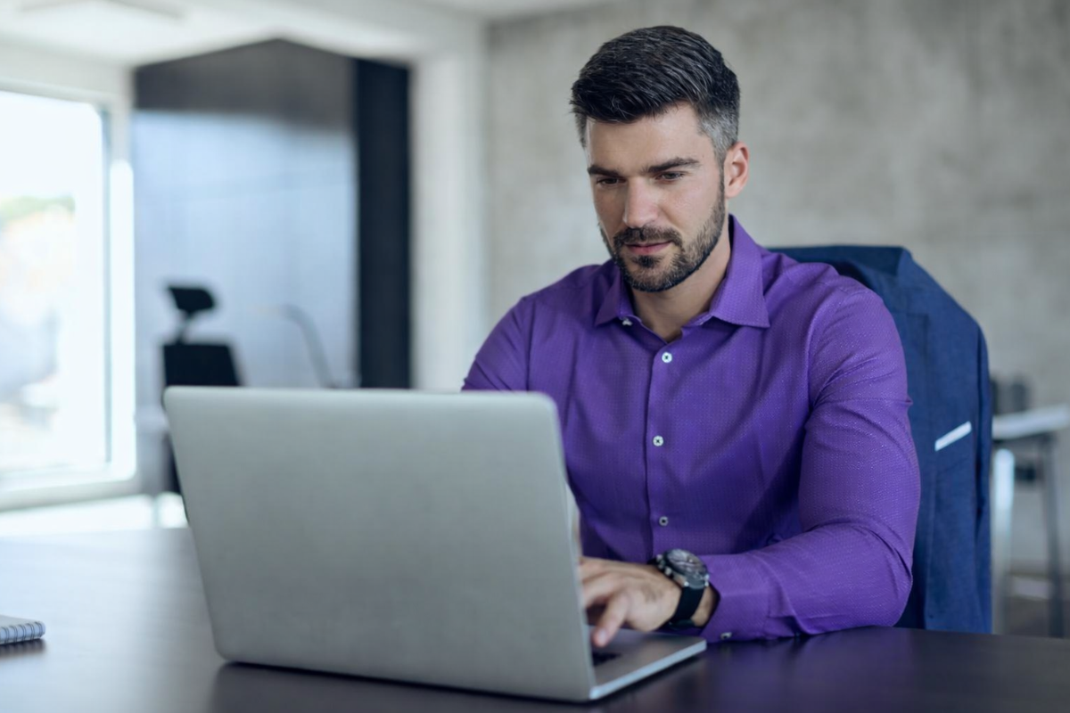Homem profissional trabalhando em um notebook sobre uma mesa em um ambiente de escritório representando: Tributação no destino: o impacto da mudança em toda cadeia da microempresa.