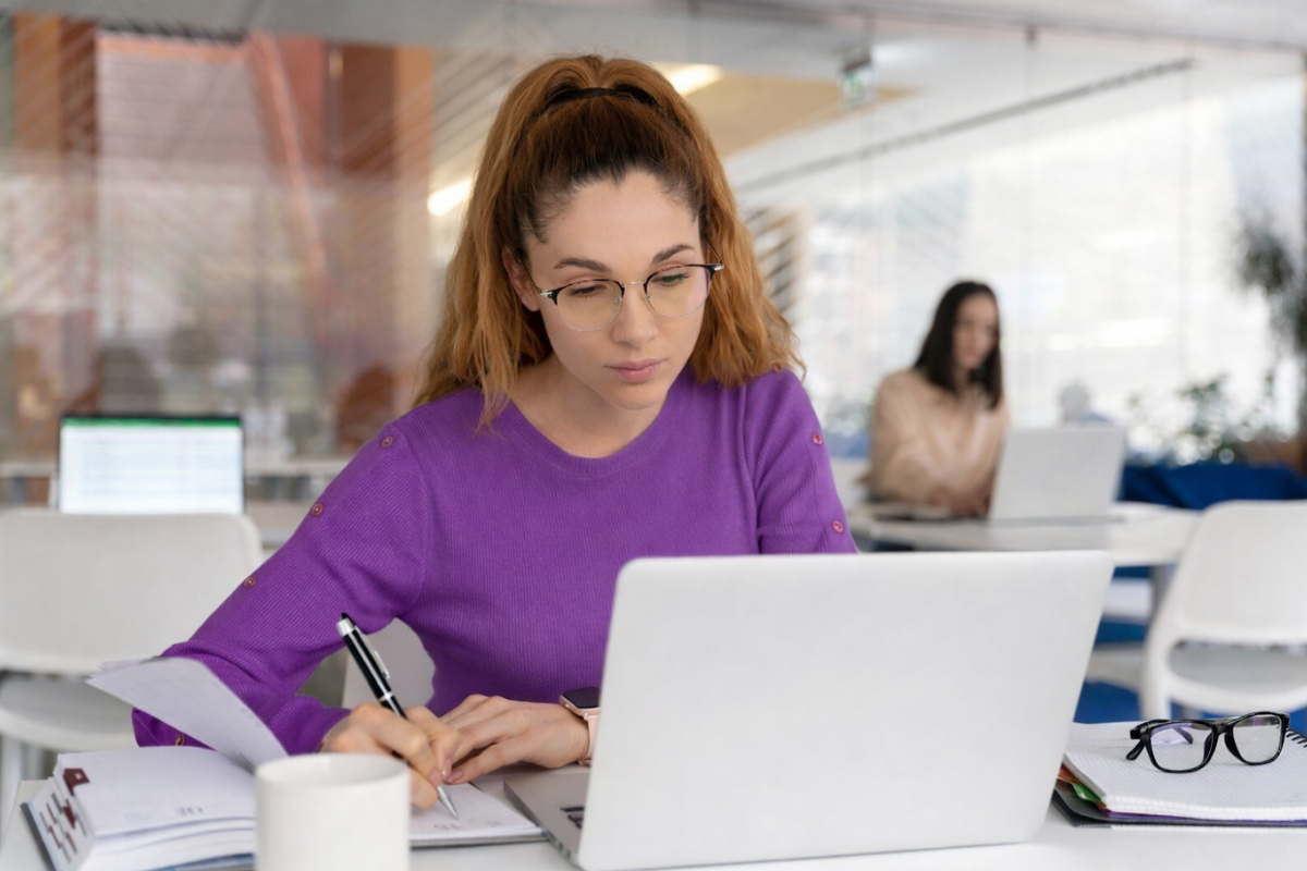 Mulher profissional trabalhando em um notebook sobre uma mesa em ambiente de escritório representando: O que muda na nota fiscal com o IBS, CBS e IS?