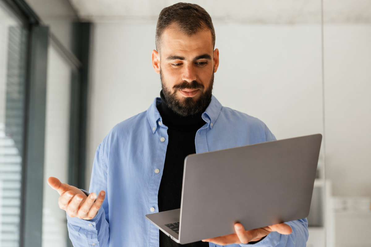 Homem andando usando um notebook em ambiente de escritório representando: Planilhas ou sistema de gestão: qual é melhor para microempresas?