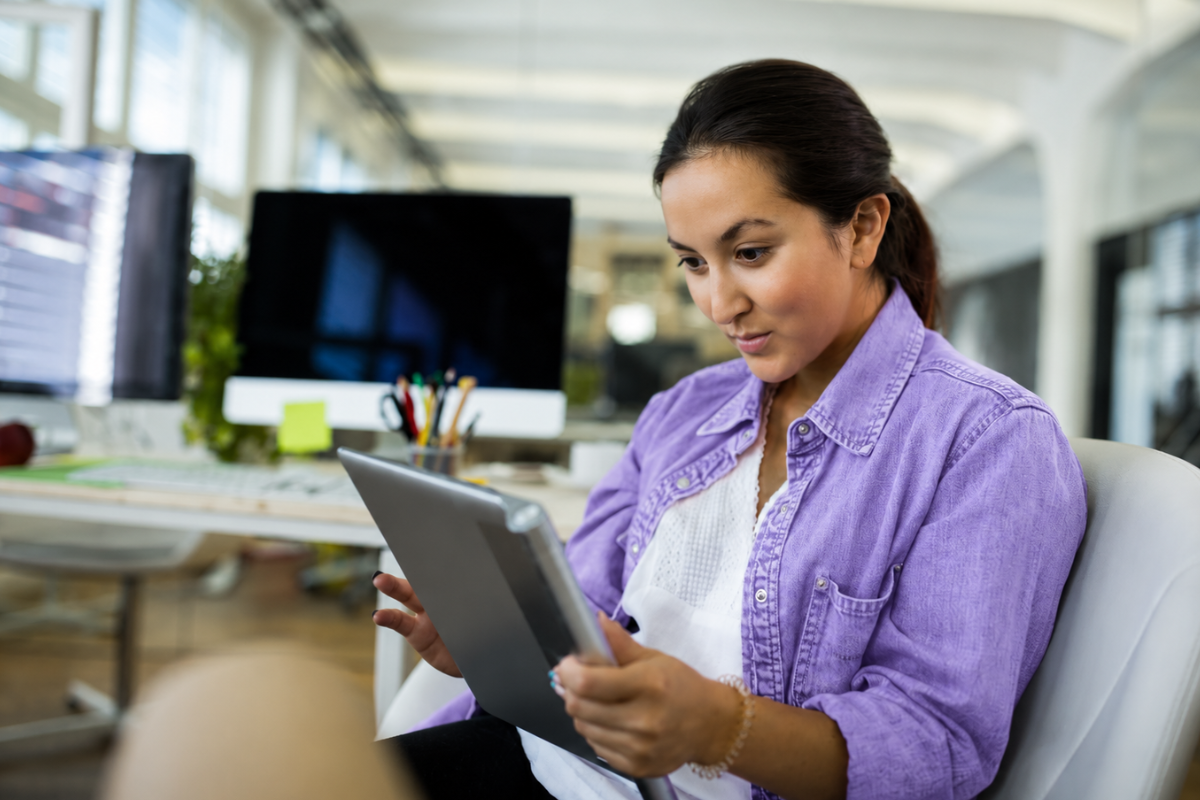 Mulher usando tablet com uma mesa ao lado e um computador sobre a mesma representando: Um ERP reduz o risco de autuação?